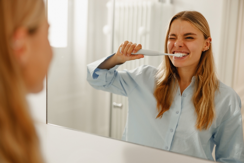 A woman brushing her teeth with an electric toothbrush in a bathroom mirror