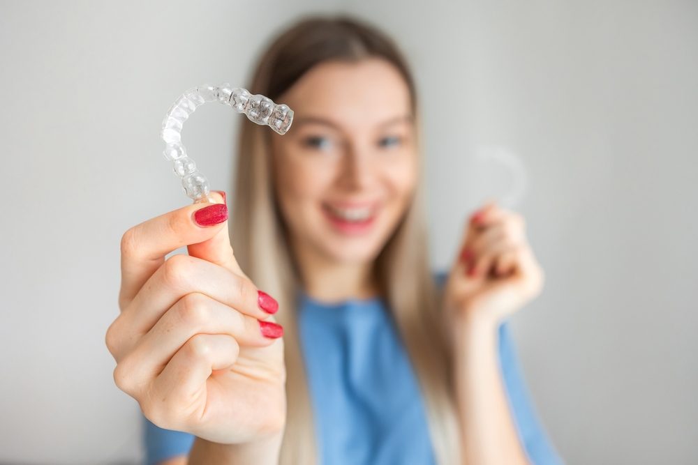 A smiling woman holding a transparent dental aligner in the foreground
