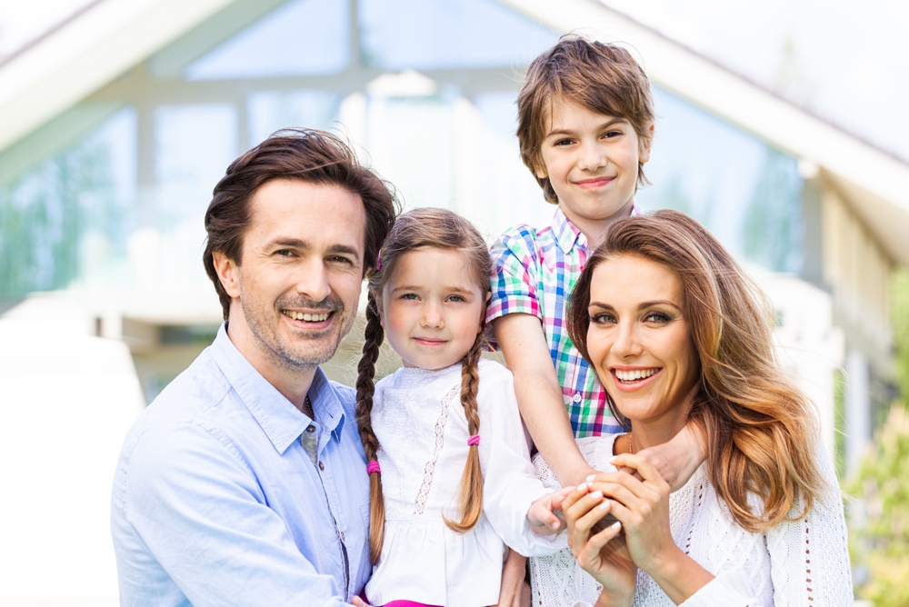 A family of four smiling together outside a home