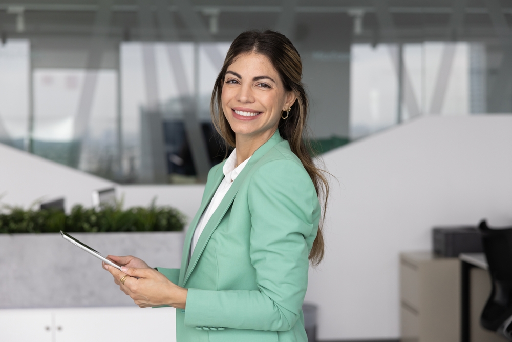 A smiling woman in a mint-green blazer holding a tablet