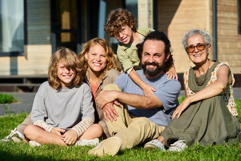 A multigenerational family of five smiling together on a lawn outside a home