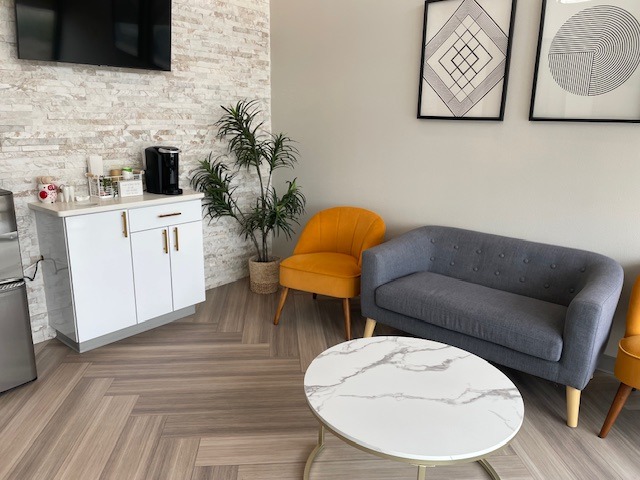 Waiting area with a gray sofa, yellow chairs, a round coffee table, and a beverage station