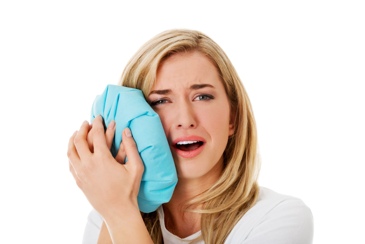A woman holding a cold compress against her cheek to ease tooth pain