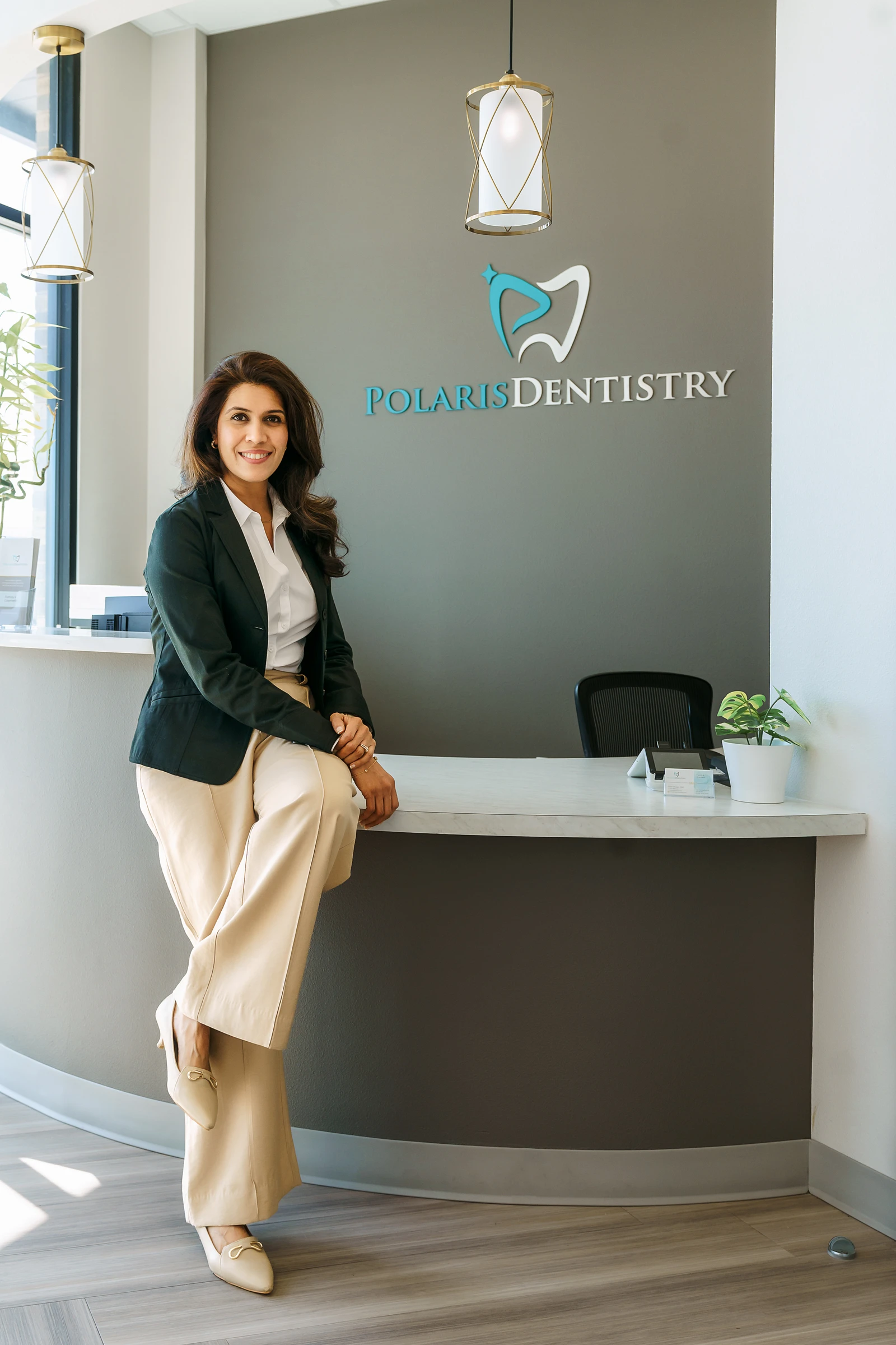 Dr. Shilpa Dhawan seated at the reception desk beneath the Polaris Dentistry sign